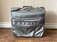Front view of green-grey Briggs & Riley rolling wardrobe bag with front zippered pocket.