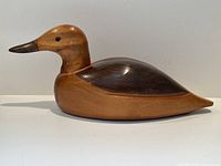 Side view of the carved wood duck decoy showing the body, neck, and head profile with distinct natural wood grain.