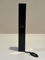 Full front view of slim black rectangular box with gold Christian Louboutin script logo in center.