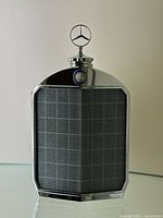 Front view of chrome plated radiator-shaped decanter bottle on glass surface with neutral background