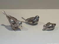 Group view of three silver plated bird figurines