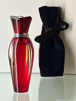 Front view of red glass perfume bottle next to velvet pouch