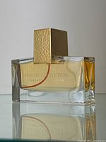 Side-on view of rectangular clear glass perfume bottle showing amber liquid, Private Collection label, gold-tone textured square cap
