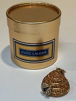 Gold cylindrical Estee Lauder box and closed bee hive compact side by side