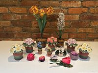 Full frontal view of floral decor lot showing all ceramic flower sculptures and fabric pincushions arranged neatly against brick wall background on white surface.