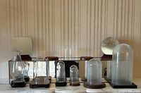 Metal and glass mirrored display shelf with seven various glass display domes and two small rectangular mirrors. View shows full lot arranged in front of a striped wallpaper.