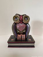 Front view of colorful hand-painted owl wooden sculpture on decorative base showing detailed eyes and chest design.