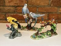 Three English porcelain bird figurines by Stangl, hand-painted, showing colorful birds on naturalistic bases with flowers and leaves.