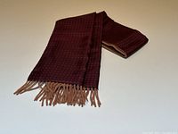 Folded burgundy scarf with small dot pattern and camel fringes on a white background.