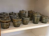 Set of 10 green glaze Irish Wade porcelain egg coddlers with lids displayed on shelf.