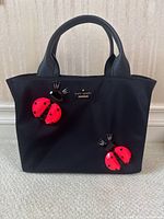 Front view of black tote with two red ladybug appliques and Kate Spade logo