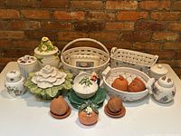 Front view of assorted ceramic kitchenware including jars with floral lids, ceramic baskets, leafy serving bowls, terracotta pomegranate containers, and decorative items.