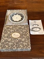Porcelain cake stand in original packaging, showing the top tier plate and box with Femme Marcel Rochas label.