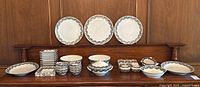 Full display of serving lot on wooden bench with large plates at back and various bowls, platters and plates below