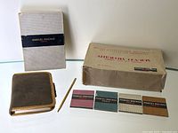 Photo of the green suede notebook, gold-toned pencil, white box, and 16 matchbooks in original carton