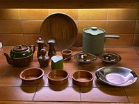 Full lot view showing all items including wooden bowl, Denby pot, nut dishes, salt and pepper shakers, creamer, teapot and condiment dishes arranged on tiled surface against wood and tile backsplash.