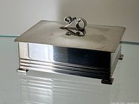 Closed rectangular silver-plated box with stepped base and scroll handle, front/side view.