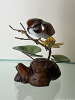 Side view showing the enamel sparrow on a metal branch with green leaves and a yellow flower atop a naturalistic brown base.