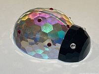 Faceted iridescent glass ladybird viewed from back, showing multicolored facets, red crystal spots, and Oleg Cassini signature.