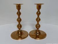 Front angle view of a pair of brass candlestick holders showing their polished finish and rounded baluster designs.