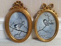 Pair of two oval gilt wood frames with chickadee prints shown side by side against a striped wallpaper background.