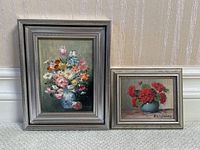 Pair of vintage framed oil paintings side by side on carpet with wallpapered wall background