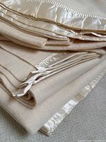 Close-up of folded blankets showing cream wool fabric and ivory satin trim