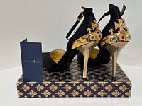 Pair of black satin stilettos on branded shoebox with informational card
