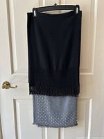 Photo of two shawls hanging on hanger against white door. Black shawl on top with beaded fringe and gray shawl below with rhinestone decoration and fringed edges.