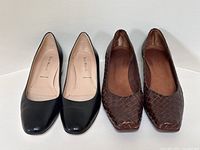 Front view of both pairs showing black smooth leather pumps alongside brown woven leather pumps