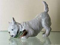 Side-angle view of the white ceramic West Highland Terrier dog figurine in a playful pose with front paws on a shoe showing wear on one ear.