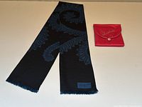 Full view of black silk scarf with blue paisley pattern beside pink satin pouch on white surface.