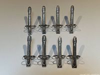 Top-down view showing all eight silver plated asparagus tongs arranged in two rows with asparagus motif handles.