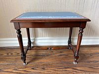 Front view of the antique walnut bench showing blue upholstered seat with pink trim and turned legs with casters.