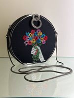 Front view of circular clamshell purse featuring crystal hand holding bouquet and chain strap
