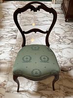 Front view showing carved balloon back and green upholstered seat with wreath and bee patterns.