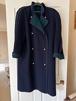 Front view of navy blue double-breasted wool coat with gold-tone buttons and green interior trim