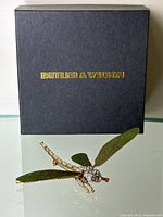 Original black Butler & Wilson box with gold logo and matching dragonfly brooch displayed on glass surface