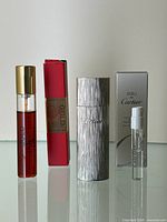 Three perfume bottles and red box displayed, showing the Must de Cartier Gold Eau de Parfum bottle and two smaller Eau de Cartier bottles with refillable travel holder.