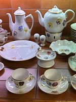 Close-up of coffee pot, tea pot on warmer, large round platter, scalloped bowl, pedestal dish, salt and pepper shakers, cups and saucers.