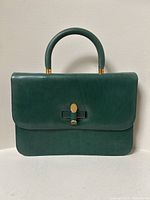Front view of emerald green leather handbag showing flap, handle, and turn-lock closure