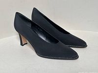 Side view of black pointed-toe heeled shoes with rhinestone edging on the front and low curved wooden heels.