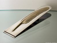 Angled view of the desk clip showing the gold plated feather on the silver base with smooth polished finish and flat clip edge.