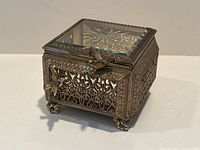 Front-right perspective showing filigree sides, bird latch and hinged glass lid