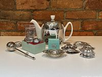 Full lot displayed on white table against brick wall, showing teapot center with various strainers and infusers spread around
