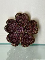 Front view of the gold-toned floral brooch covered with small purple rhinestones and gold metal outlining the petals.