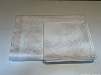 Folded damask tablecloth and dinner napkins showing the woven lily of the valley floral pattern and fabric texture.