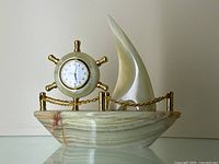 Front view of the carved onyx sailboat desk clock showing the boat, sail, and ship wheel clock face with gold-tone chain and posts
