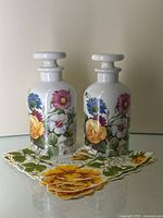 Pair of floral porcelain bottles with stoppers standing on a floral handkerchief on glass surface