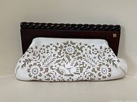 Front of vintage white cutout leather clutch with floral and bird detail on beige backing, wooden frame with twisted carving, brass R emblem.